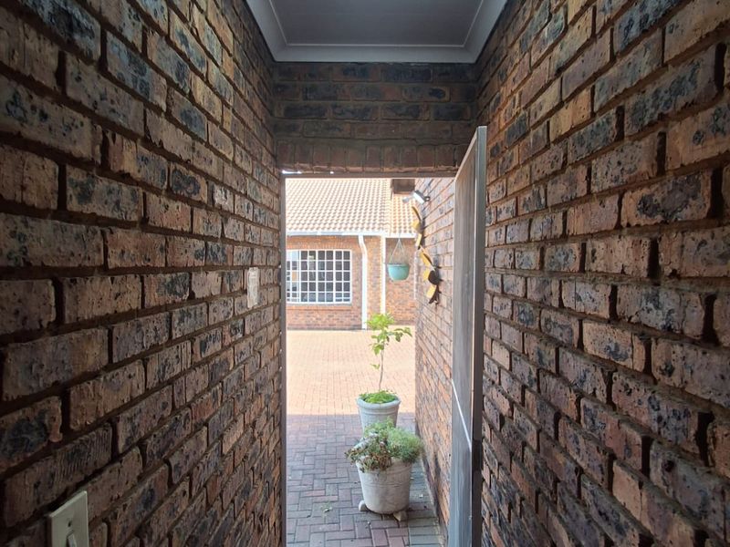 A narrow hallway featuring exposed brick walls and tiled flooring, leading directly to an outdoor paved courtyard area.