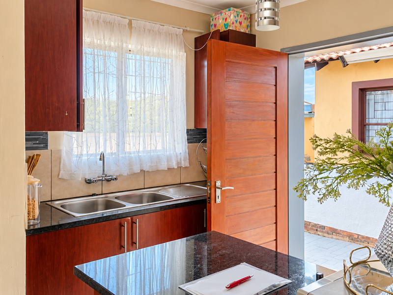 A functional kitchen featuring dark wood cabinetry, granite countertops, and a double stainless steel sink, with direct access to an outdoor patio area.