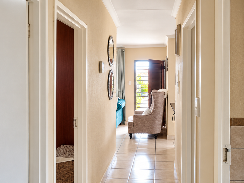 A bright hallway featuring tiled flooring and coved ceilings, providing access to multiple rooms and leading towards an exterior security gate.