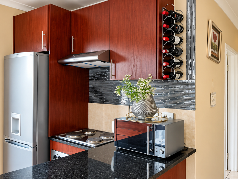 Compact kitchen featuring dark wood cabinetry, granite countertops, a built-in wine rack, and a modern tiled backsplash with integrated electric hob and extractor fan.