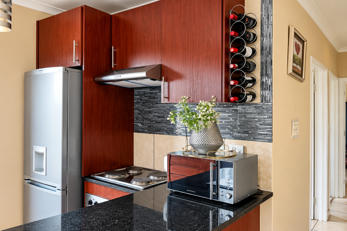 Compact kitchen featuring dark wood cabinetry, granite countertops, a built-in wine rack, and a modern tiled backsplash with integrated electric hob and extractor fan.