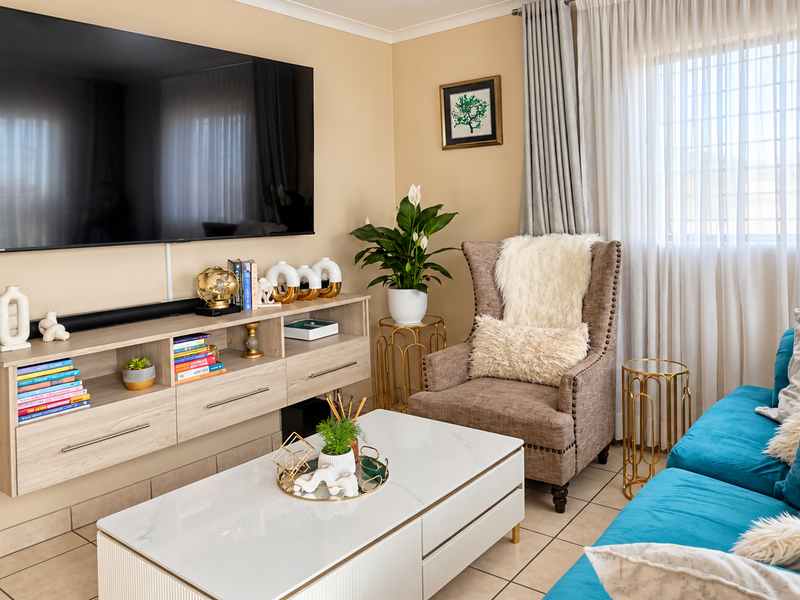 A well-maintained living room featuring tiled flooring, neutral wall tones, and a window fitted with security bars.