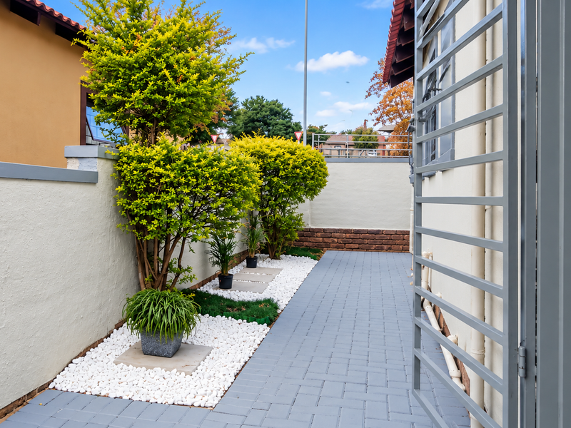 A well-maintained side passage featuring grey paved flooring, a secure metal gate, and a neat garden bed with white pebble landscaping.