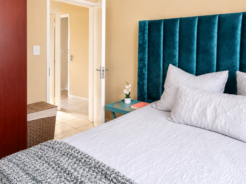 A well-maintained bedroom featuring a built-in wardrobe, neutral wall tones, and tiled flooring, with an open doorway leading to an adjacent hallway.