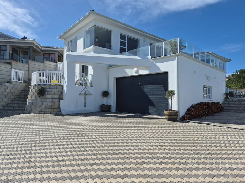 Modern two-story house exterior featuring a paved driveway, automated garage, and an upper-level balcony with glass balustrades.