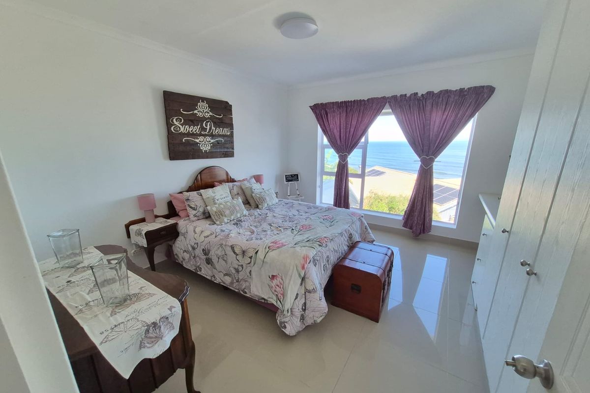 A bright bedroom featuring large windows with ocean views, neutral tiled flooring, and built-in storage, offering a clean and well-maintained living space.