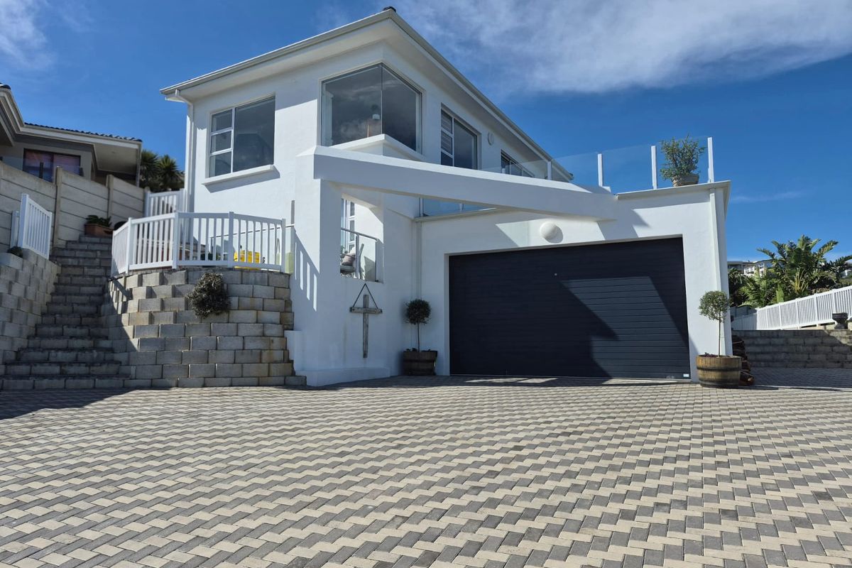 Modern two-story home exterior featuring a paved driveway, integrated garage, and elevated balcony with glass balustrades.