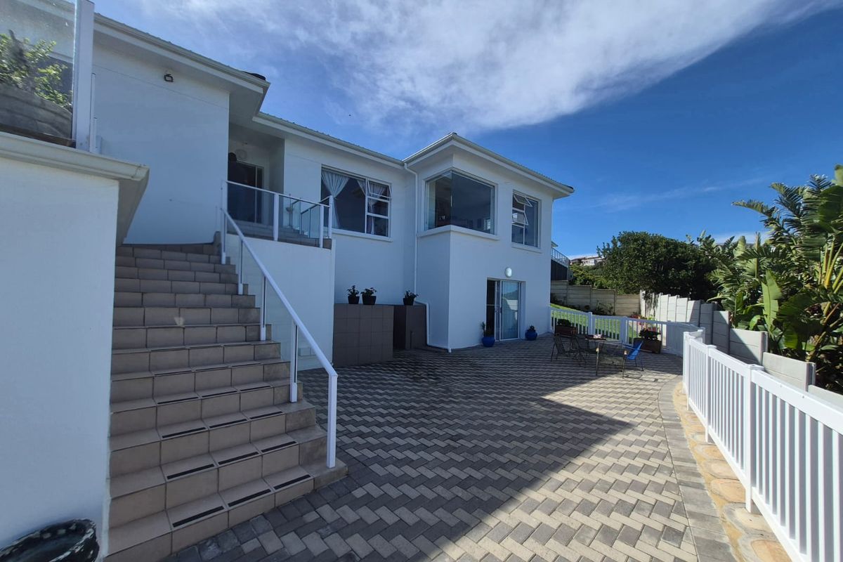 A well-maintained rear exterior featuring a paved patio area, external staircase with glass balustrades, and a white picket fence bordering the garden.