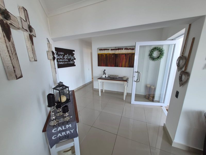 A bright and welcoming entrance hall featuring neutral tiled flooring and a modern glass panel front door.