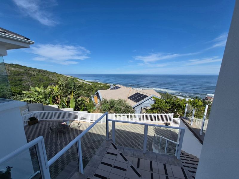 Elevated outdoor view featuring a tiled patio, glass balustrades, and a scenic coastal outlook with solar panels visible on the neighboring roof.