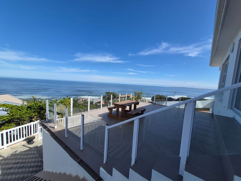 Spacious elevated balcony featuring a modern glass balustrade and tiled flooring, offering expansive ocean views.