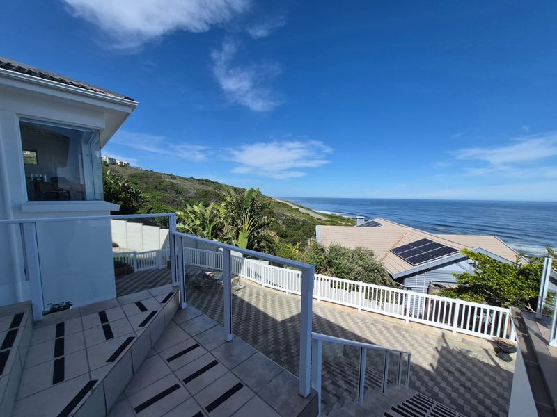 A spacious outdoor balcony featuring a modern glass balustrade and tiled flooring, offering expansive coastal and ocean views.