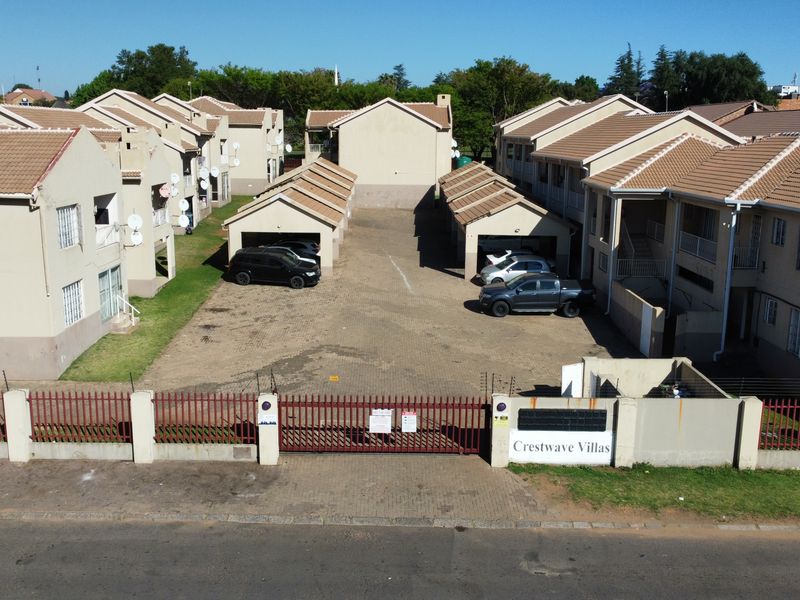 Aerial view of Crestwave Villas townhouse complex featuring multiple residential units, paved driveway, carports, and secure perimeter fencing.