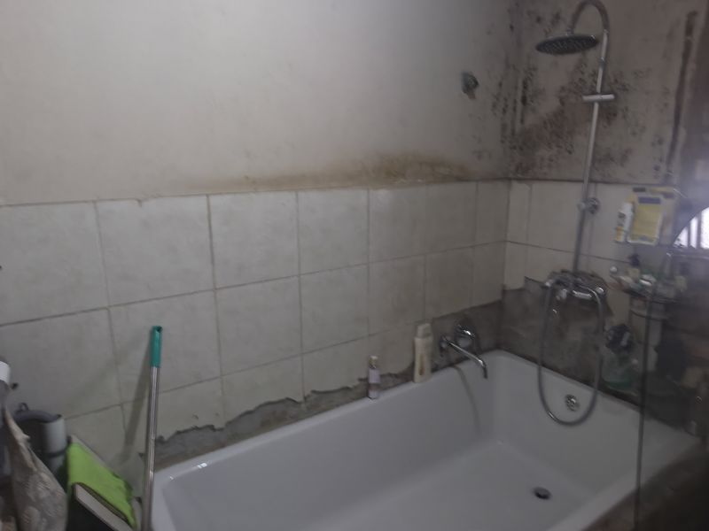 Bathroom featuring a bathtub with shower attachment, tiled walls, and exposed brickwork. The space requires significant maintenance and renovation due to visible wall damage.