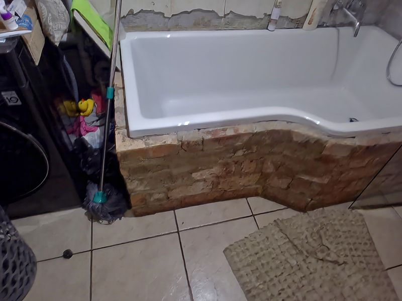 Bathroom featuring a bathtub with a brick surround and glass shower screen, currently requiring wall repairs and finishing to improve the overall aesthetic.