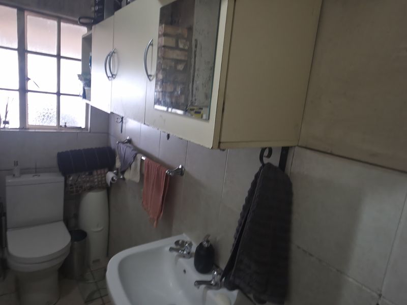 A functional bathroom featuring a toilet, washbasin, and wall-mounted cabinetry, with tiled finishes throughout. The space would benefit from cosmetic updates.