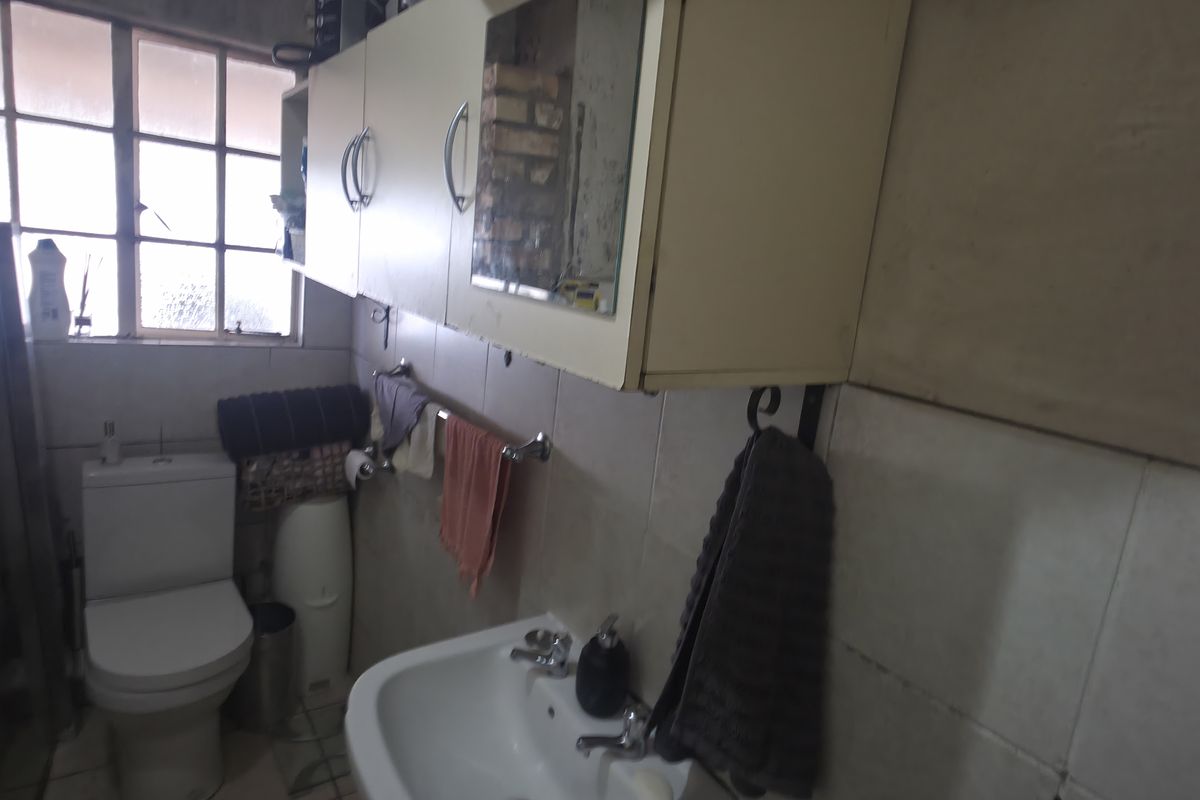 A functional bathroom featuring a toilet, washbasin, and wall-mounted cabinetry, with tiled finishes throughout. The space would benefit from cosmetic updates.