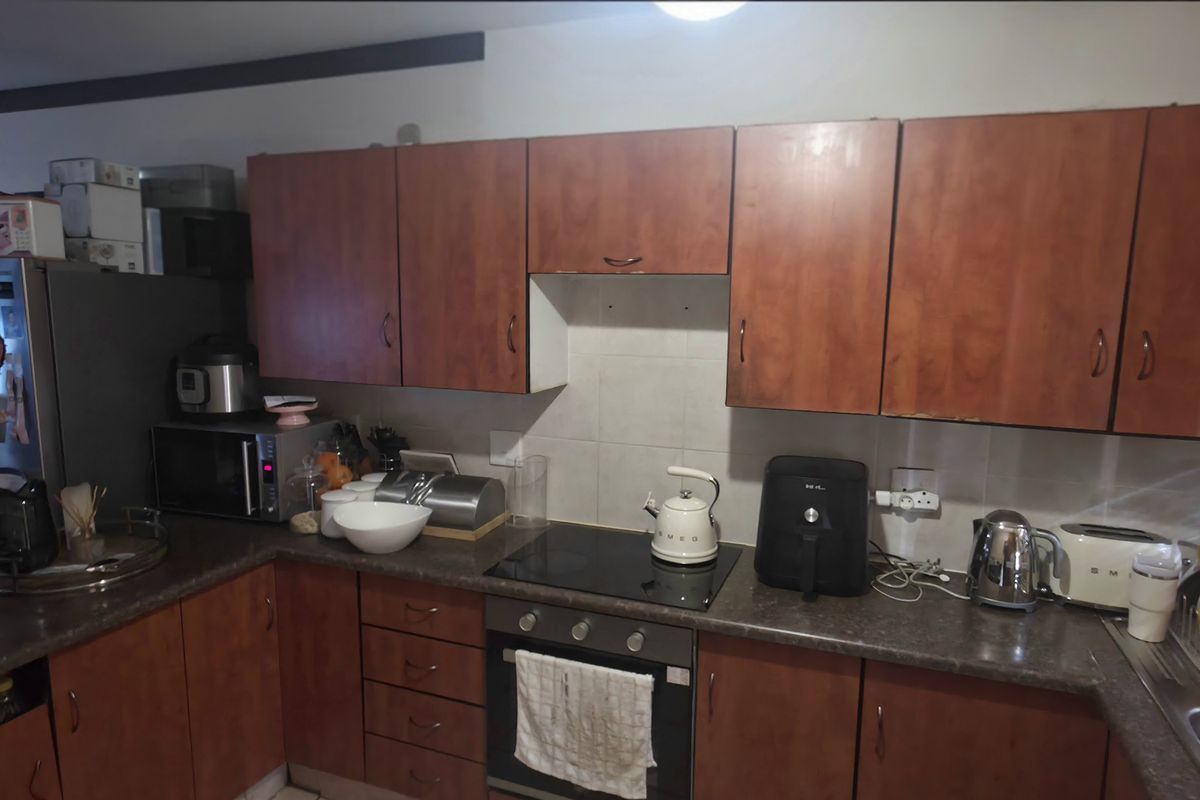 A functional kitchen featuring wood-look laminate cabinetry, dark countertops, a built-in oven, and an electric hob with a tiled backsplash.