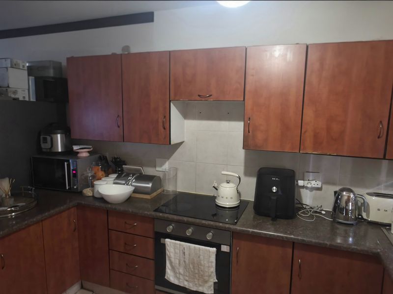 A functional kitchen featuring wood-look laminate cabinetry, dark countertops, a built-in oven, and an electric hob with a tiled backsplash.
