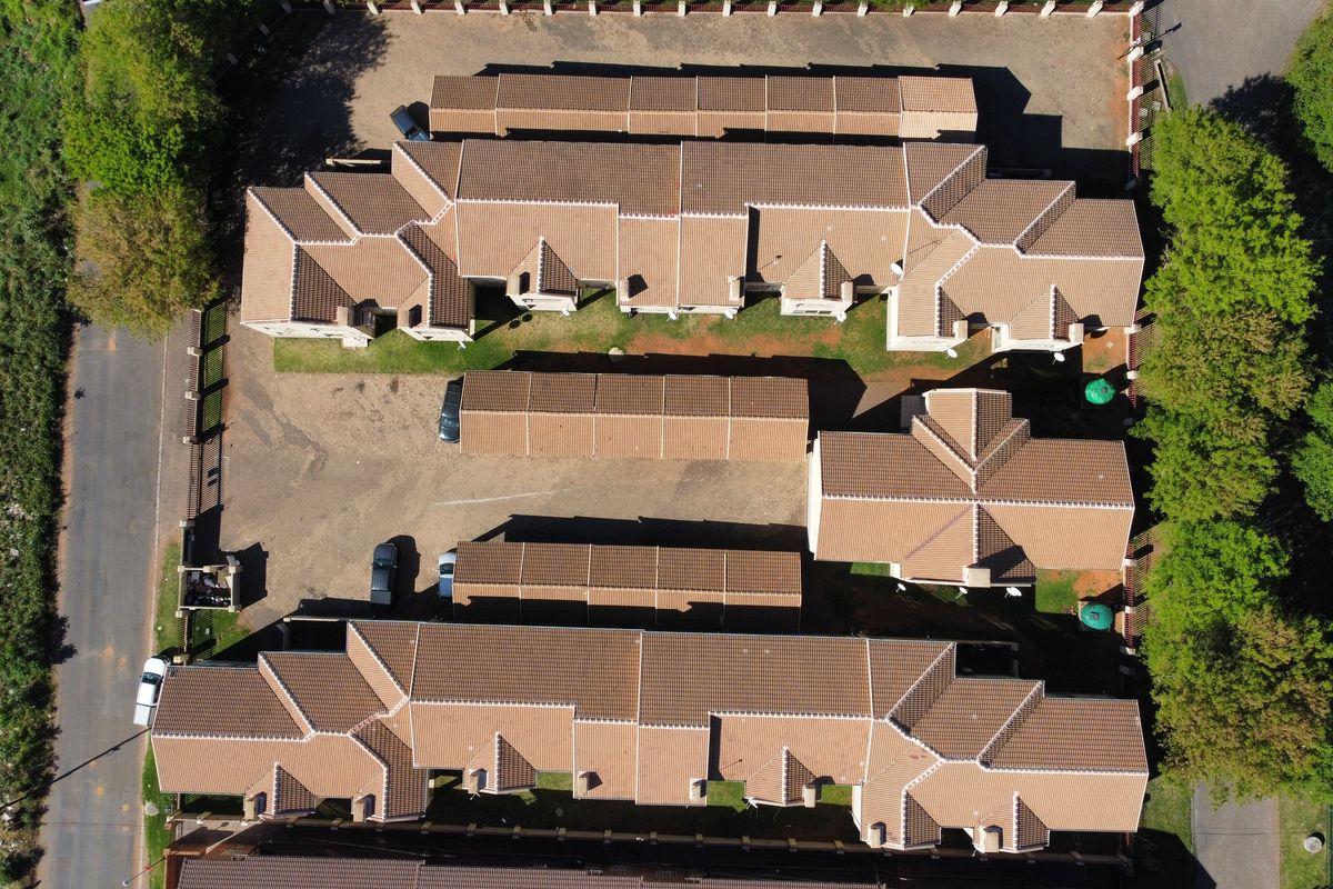 Aerial view of a townhouse complex featuring multiple residential units with tiled roofs, paved driveways, and surrounding landscaped garden areas.
