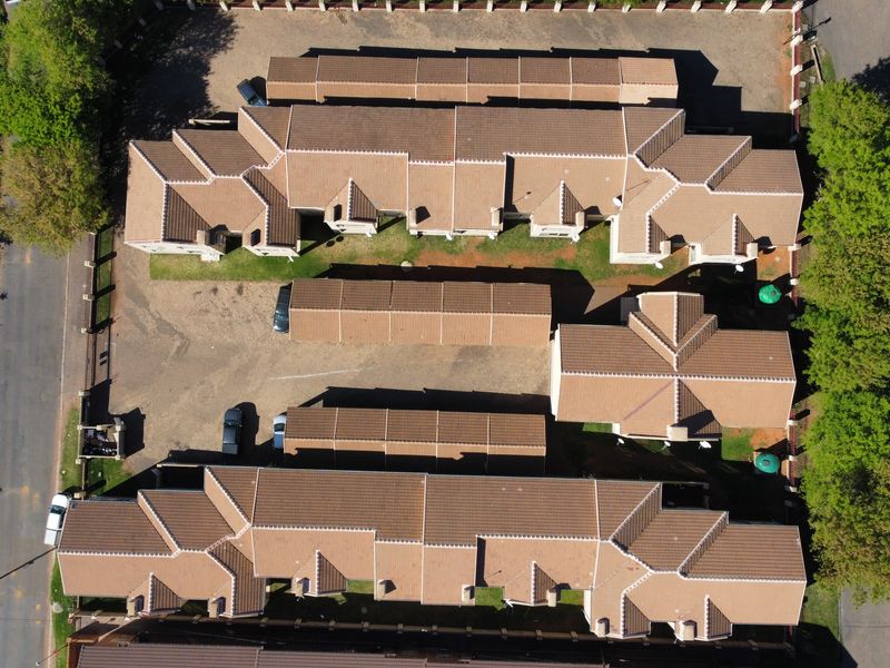 Aerial view of a townhouse complex featuring multiple residential units with tiled roofs, paved driveways, and surrounding landscaped garden areas.