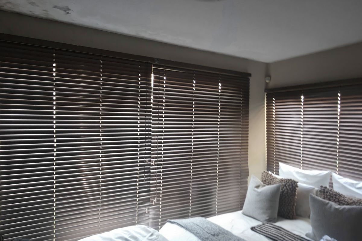 A bedroom featuring dark venetian blinds and visible water staining on the ceiling, indicating potential maintenance requirements.