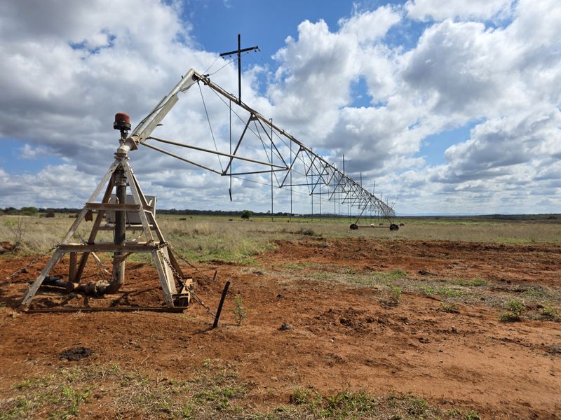 A large-scale center pivot irrigation system situated on open farmland, showing signs of age and maintenance requirements.
