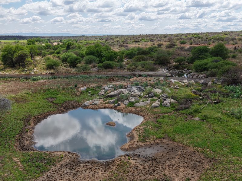 A scenic elevated view of the farm landscape featuring a natural pond, rock formations, and surrounding vegetation under a cloudy sky.