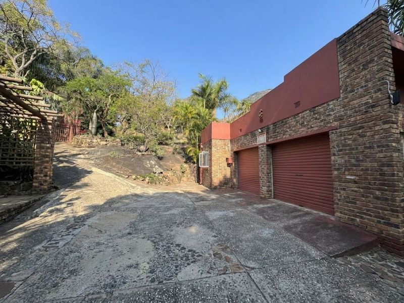 A double garage with roller doors and a face brick exterior, featuring a sloped concrete driveway and established garden surroundings.