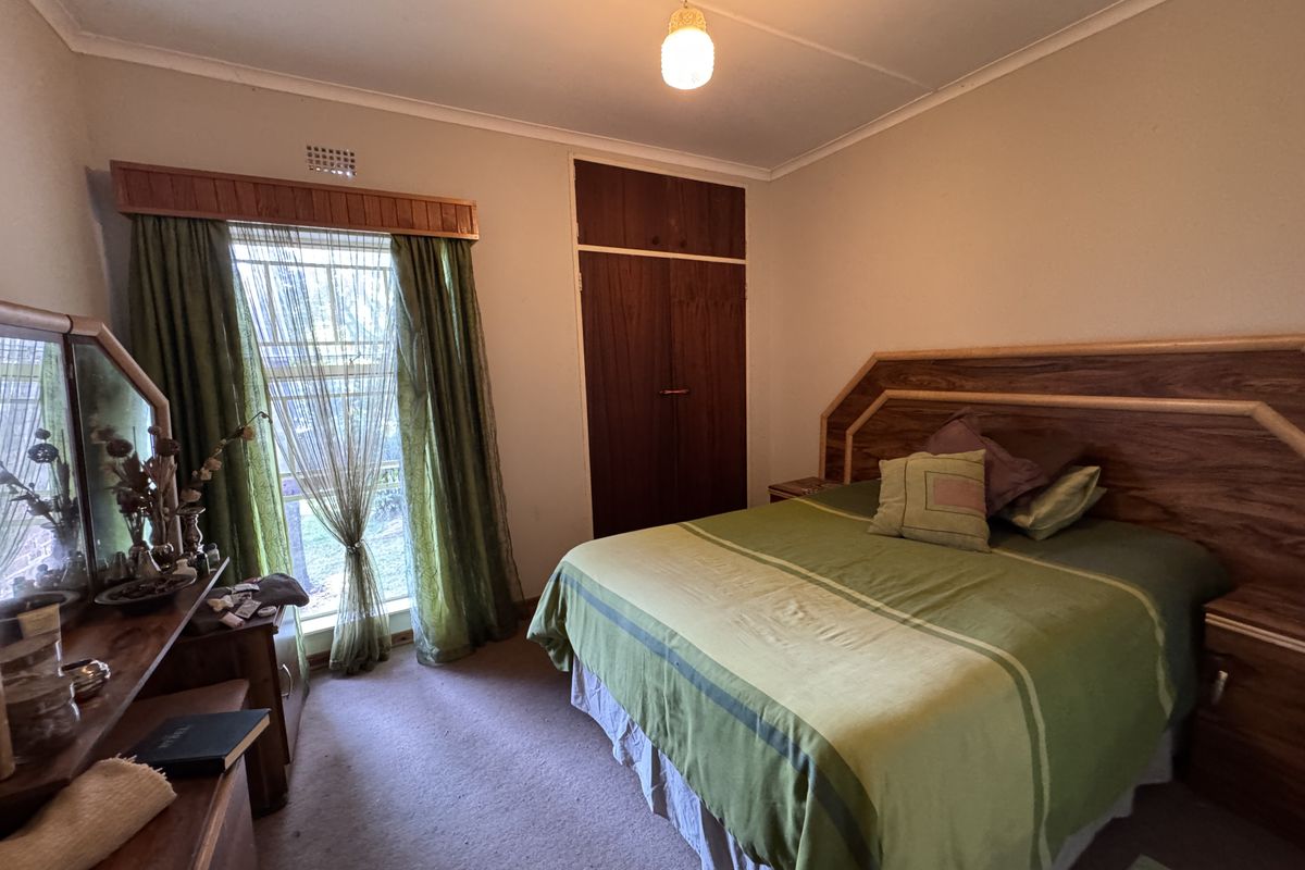 A bedroom featuring carpet flooring, a built-in wardrobe, and a window with a wooden pelmet.