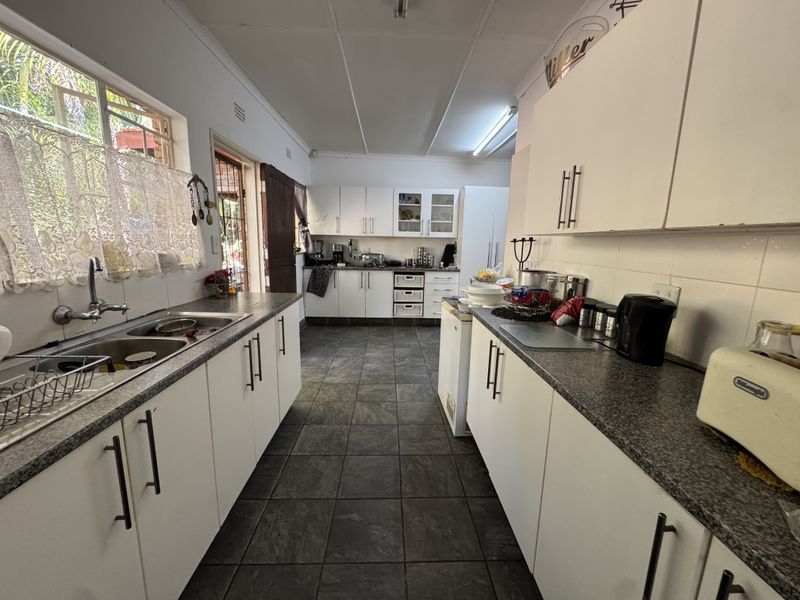 A functional kitchen featuring white cabinetry, dark laminate countertops, double basin sink, and tiled flooring with direct access to the exterior.