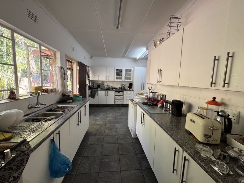 A functional galley-style kitchen featuring white cabinetry, laminate countertops, double basin sink, and tiled flooring with natural light from a large side window.