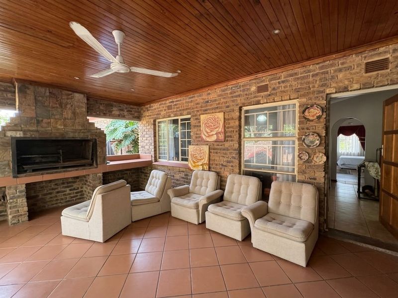 Covered patio area featuring exposed brick walls, a built-in braai, timber ceiling with fan, and tiled flooring, offering a functional outdoor entertainment space.