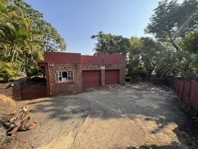 A detached double garage featuring a brick facade, roller shutter doors, and a large concrete driveway set within a mature garden.