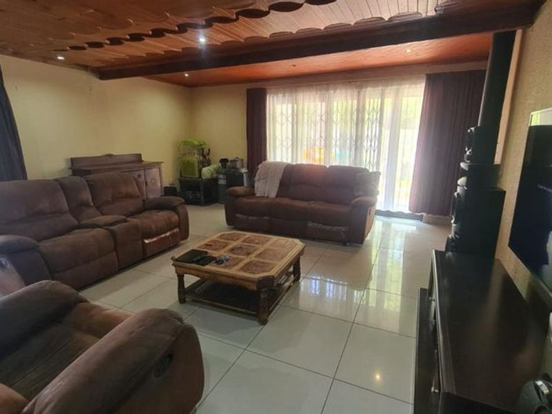 Spacious living room featuring polished tiled flooring, a distinctive wooden ceiling with recessed lighting, and large sliding glass doors leading to the exterior.