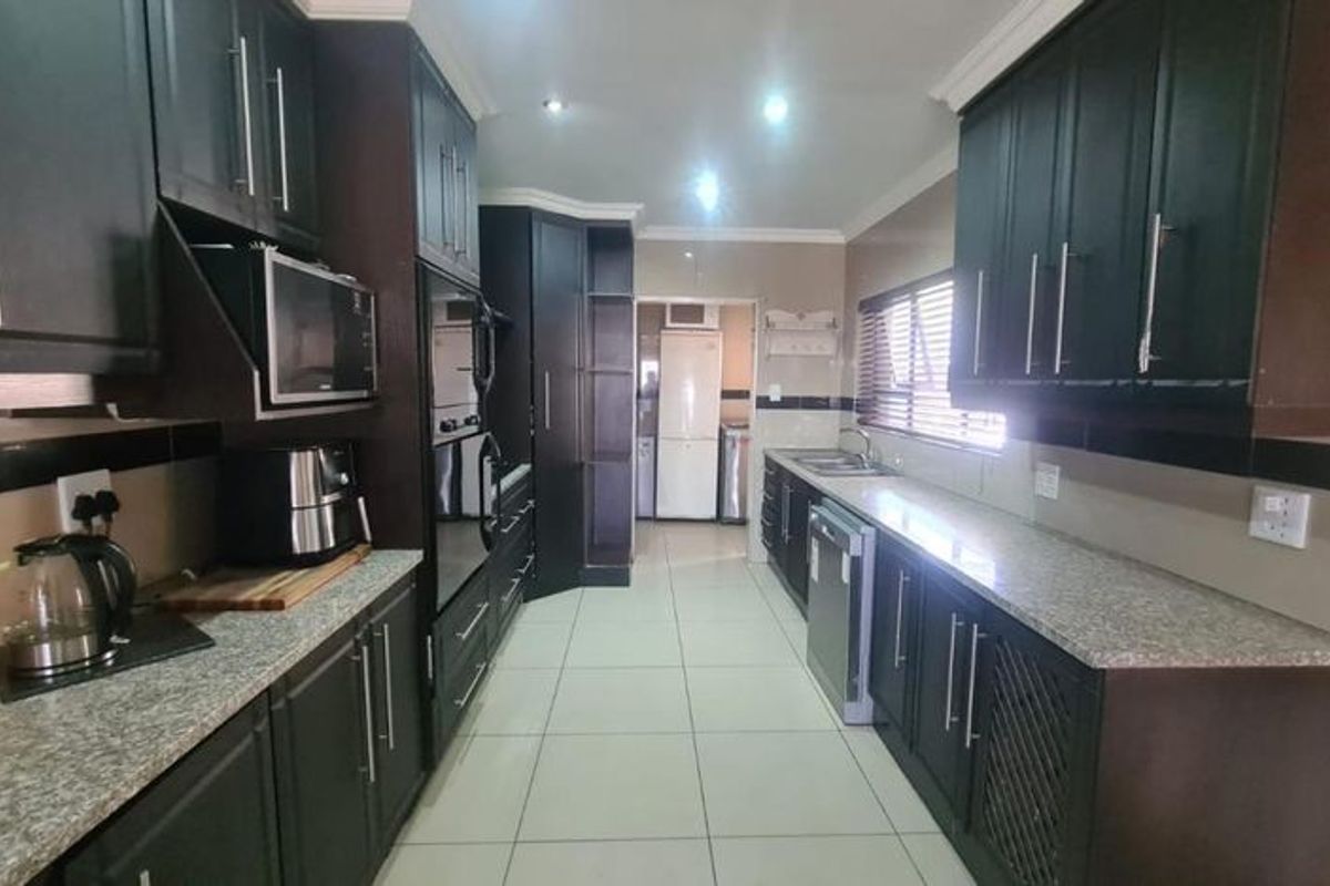A functional galley-style kitchen featuring dark cabinetry, granite countertops, integrated wall ovens, and tiled flooring with ample storage space.