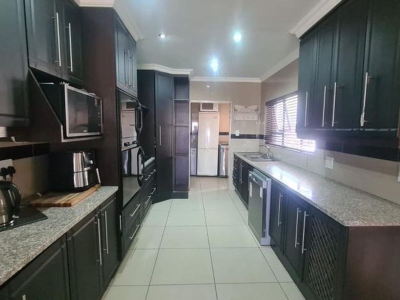 A functional galley-style kitchen featuring dark cabinetry, granite countertops, integrated wall ovens, and tiled flooring with ample storage space.