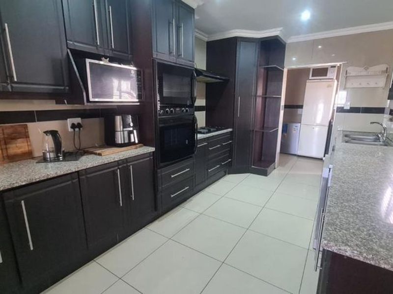 Modern kitchen featuring dark wood cabinetry, granite countertops, built-in oven, microwave, and hob, with tiled flooring and a separate scullery area.