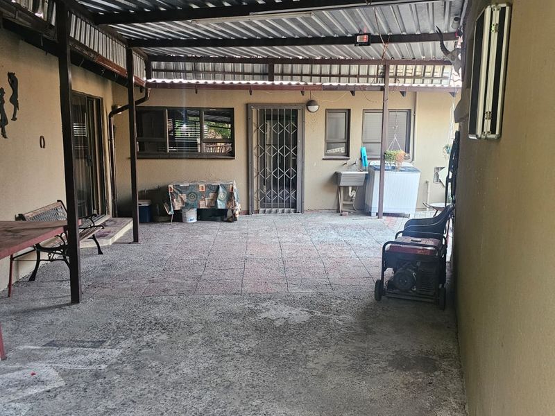 A covered outdoor patio area featuring a corrugated metal roof, tiled flooring, and an external utility sink, providing a functional space for outdoor activities.