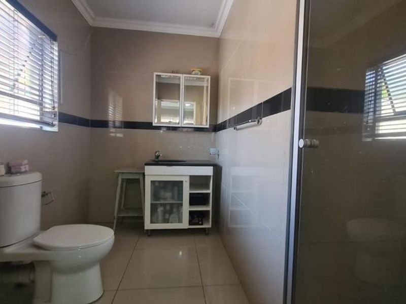 A functional bathroom featuring a vanity cabinet, toilet, and a glass-enclosed shower with neutral wall and floor tiling.