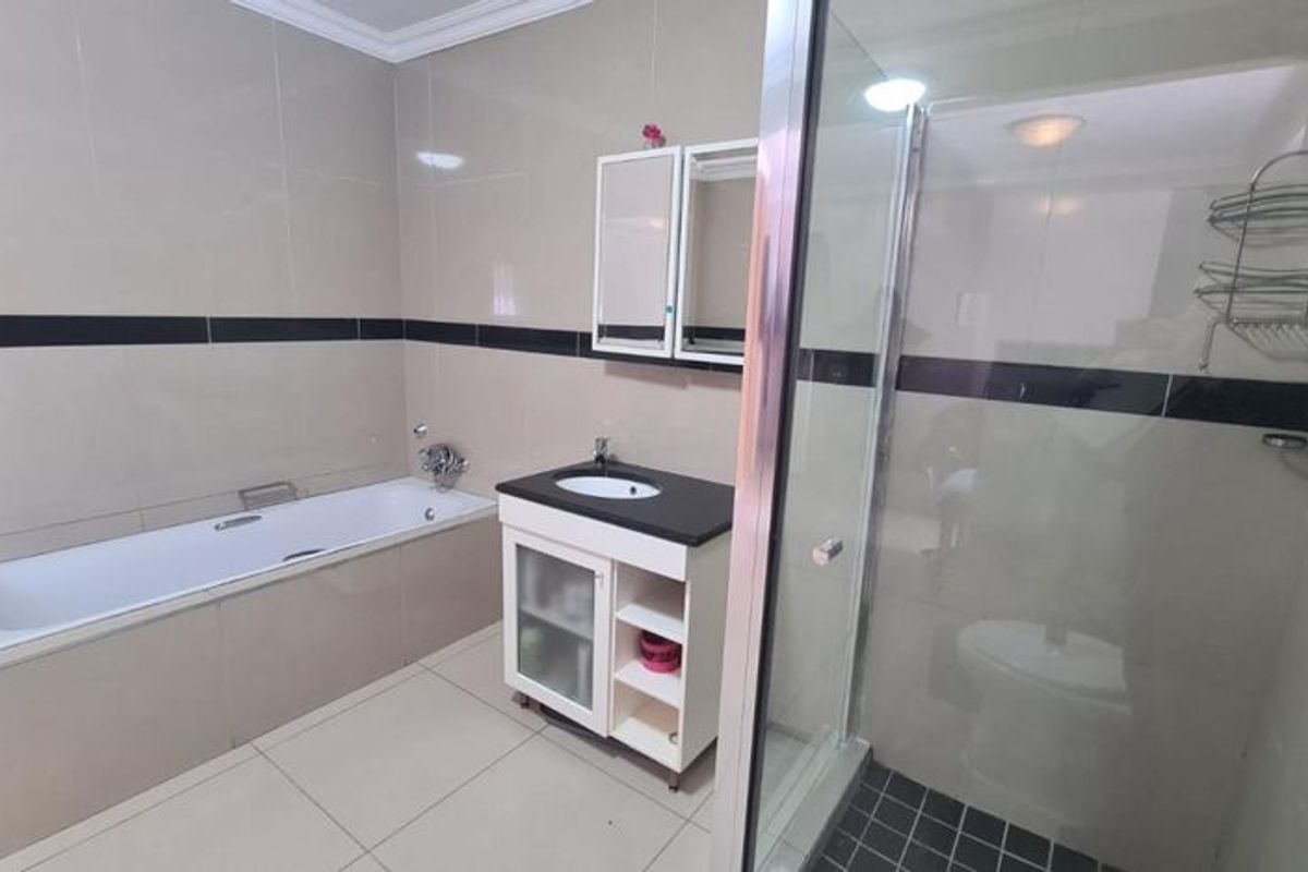 A well-maintained bathroom featuring a built-in bathtub, a separate glass-enclosed shower, and a modern vanity unit with integrated sink and storage.