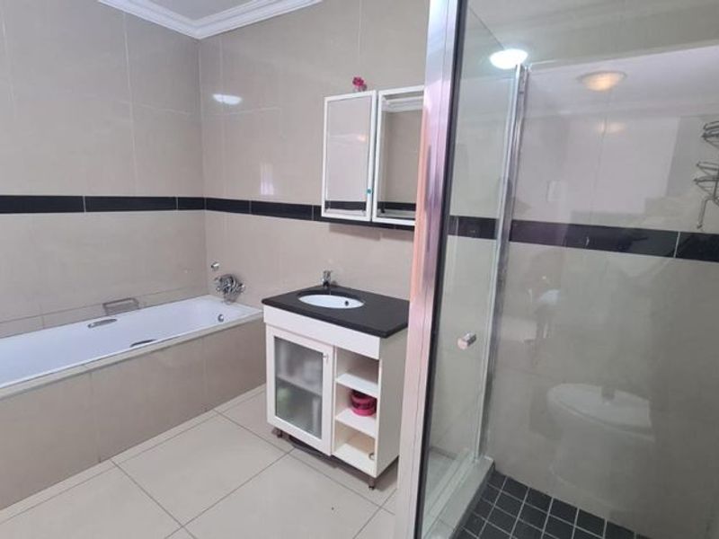 A well-maintained bathroom featuring a built-in bathtub, a separate glass-enclosed shower, and a modern vanity unit with integrated sink and storage.