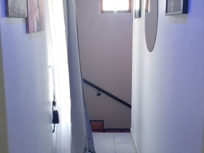 A narrow hallway featuring tiled flooring and a staircase with a handrail, leading to a small window.