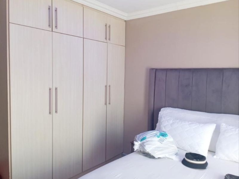 A well-maintained bedroom featuring floor-to-ceiling built-in cupboards with modern handles and decorative ceiling coving.