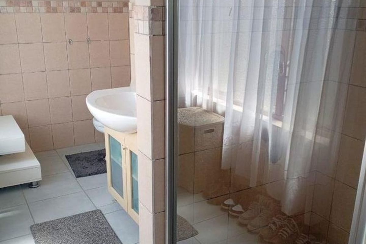A functional bathroom featuring a pedestal washbasin with vanity storage and a separate shower enclosure with tiled finishes.