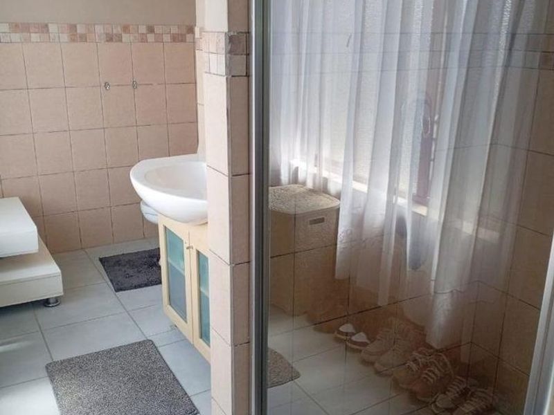 A functional bathroom featuring a pedestal washbasin with vanity storage and a separate shower enclosure with tiled finishes.