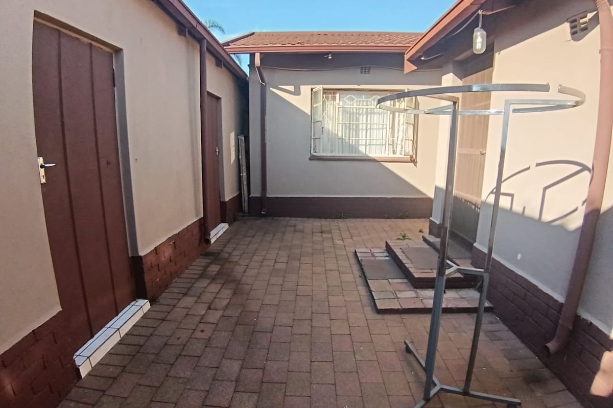 A paved rear courtyard area featuring exterior access doors, security window bars, and functional drainage downpipes.