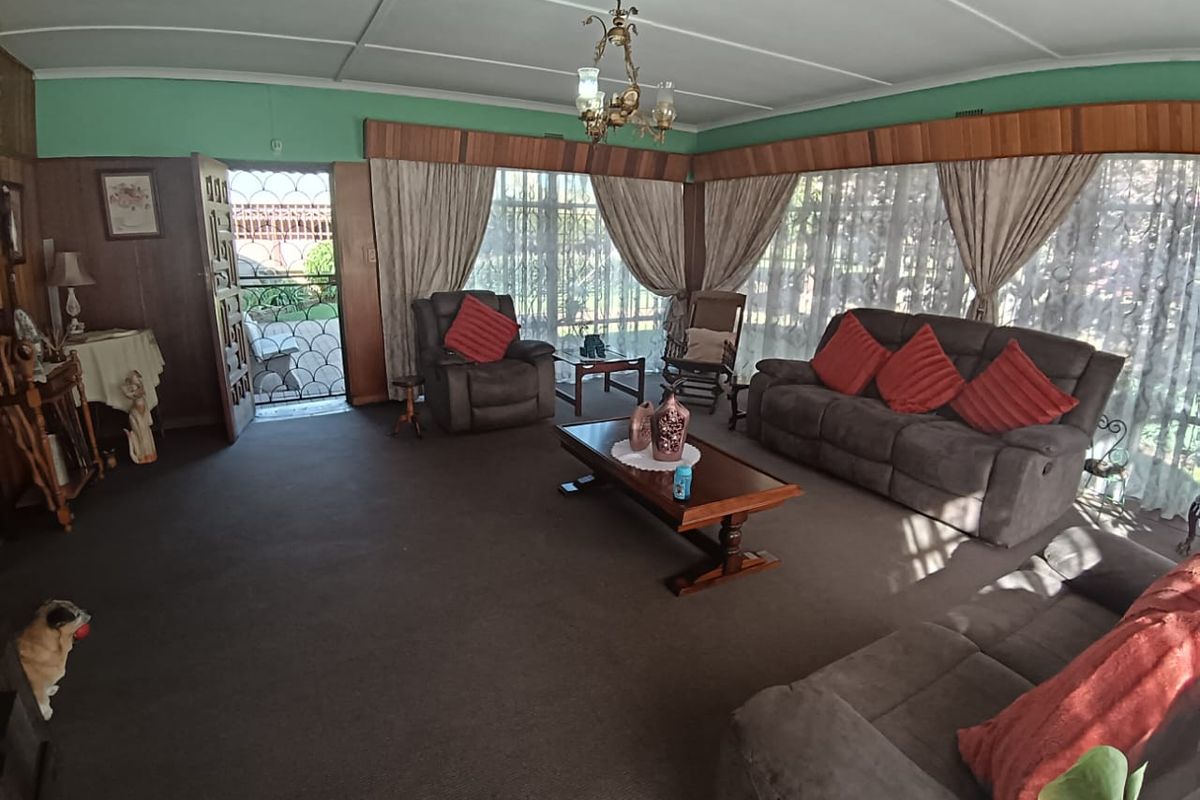 Spacious living room featuring timber wall paneling, decorative ceiling molding, and an ornate chandelier, offering a traditional aesthetic with potential for modernization.