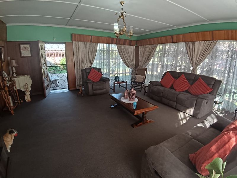 Spacious living room featuring timber wall paneling, decorative ceiling molding, and an ornate chandelier, offering a traditional aesthetic with potential for modernization.