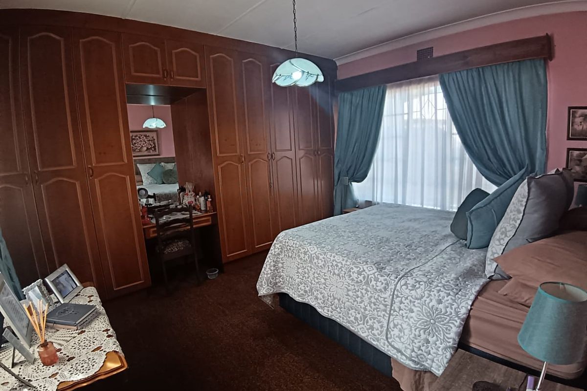 A bedroom featuring extensive built-in wooden cabinetry with an integrated vanity unit, carpeted flooring, and a window fitted with security bars.